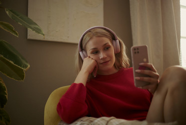Женщина в наушниках использует смартфон для электронного обучения дома - DragonImagesAsia