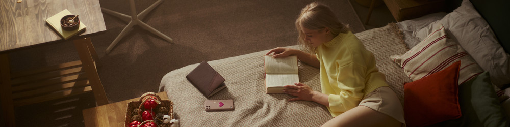 Женщина читает книгу на кровати в уютной спальне, способствуя психическому благополучию - DragonImagesAsia