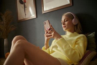 Женщина в наушниках Пользуется смартфоном, отдыхая на диване - DragonImagesAsia