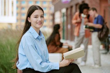 Портрет улыбается женщина, держащая книгу с различными студентами в университетском городке - AnnaStills