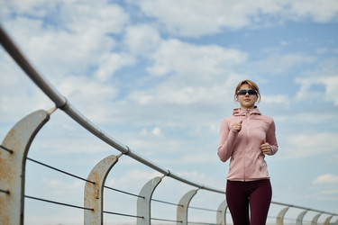 Женщина бегает трусцой по мосту во время утренней тренировки на открытом воздухе - SeventyFour