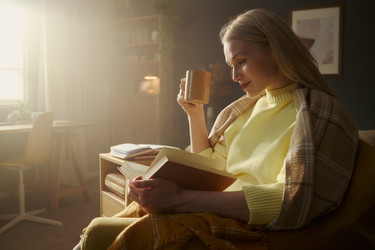 Женщина читает книгу и пьет кофе в уютной гостиной - DragonImagesAsia