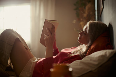 Женщина читает книгу в постели уютным утром дома - DragonImagesAsia