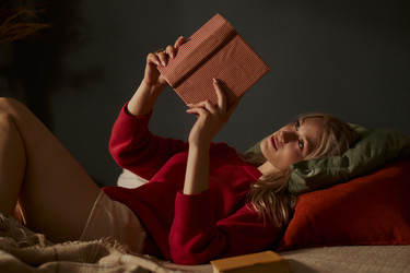 Женщина лежит на кровати и читает книгу в уютной спальне - DragonImagesAsia
