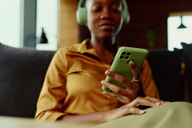 Чернокожая женщина в наушниках просматривает социальные сети на смартфоне - DragonImagesAsia