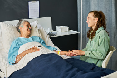 Woman Supporting Senior Patient Resting in Hospital Bed - Pressmaster