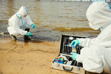 Экологи в защитных костюмах проверяют качество воды на открытом воздухе - DragonImagesAsia
