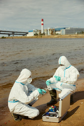 Ученые в защитных костюмах проверяют качество воды вблизи промышленного предприятия - DragonImagesAsia