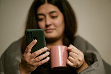 Двухрасовая женщина, пользующаяся смартфоном и держащая кофейную кружку в постели - DragonImagesAsia