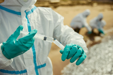 Эколог в защитном костюме берет пробы воды на открытом воздухе для исследования - DragonImagesAsia