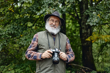 Портрет пожилого мужчины с фотоаппаратом в руках на прогулке на природе в лесу - SeventyFour