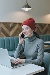 Женщина разговаривает по смартфону и работает на ноутбуке в кафе - SeventyFour