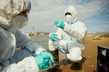 Ученые в защитных костюмах собирают пробы воды для проверки на загрязнение - DragonImagesAsia