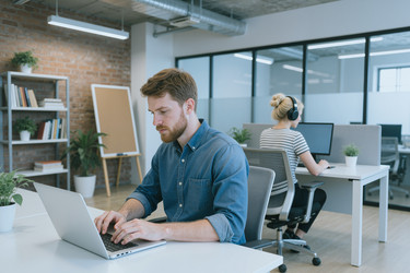 Сосредоточенный человек, работающий за ноутбуком в современном офисе с открытым пространством - SeventyFour