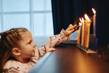 Маленькая девочка смотрит на горящие свечи Меноры во время Хануки - SeventyFour