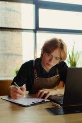 Мужчина, владелец малого бизнеса, пишет в буфере обмена рядом с ноутбуком - DragonImagesAsia