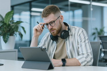 Сосредоточенный человек, работающий на цифровом планшете в современном офисе - SeventyFour