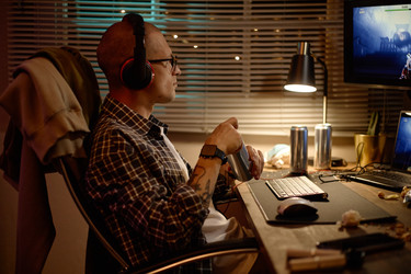 Сосредоточенный мужчина, играющий ночью в видеоигры на компьютере - SeventyFour