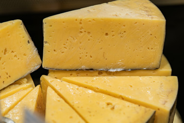 Крупным планом нарезанный желтый сыр с дырочками и дольками. Молочный пищевой ингредиент для сэндвичей, закусок, перекусов, приготовления пищи и бакалейных товаров. - Maria Moroz