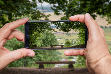 мужчина со смартфоном в руках фотографирует красивый летний пейзаж со скамейкой - Maria Moroz