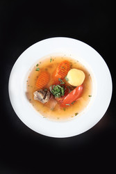 Перелейте мясной бульон в белую миску. Картофель, морковь, помидор, петрушка, кусочки говядины. Полезный домашний суп на темном фоне. Вид сверху - RusAKphoto