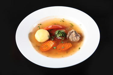 прозрачный мясной бульон с овощами в белой тарелке. перелейте мясной бульон в белую миску. картофель, морковь, помидор, петрушка, кусочки говядины. полезный домашний суп на темном фоне. вид сверху - RusAKphoto