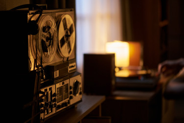 Мужчина слушает музыку с помощью винтажного катушечного магнитофона у себя дома - Mediaphotos