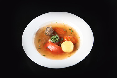 перелейте мясной бульон в белую миску. картофель, морковь, помидор, петрушка, кусочки говядины. полезный домашний суп на темном фоне - RusAKphoto