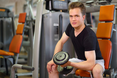 Young handsome man sits and raises dumbbell in - paha_l