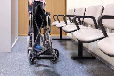 Woman folds or unfolds black wheelchair in lobby - paha_l