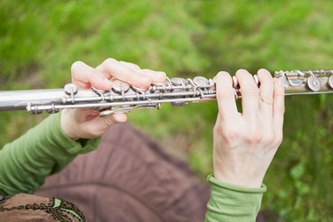 Female hands hold metal flute against green grass - paha_l
