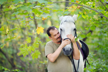 Man among leaves hugs head of white horse at - paha_l