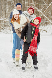 Smiling family of four stands on skates on ice - paha_l