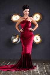 Smiling woman in red velvet dress poses near wall - paha_l