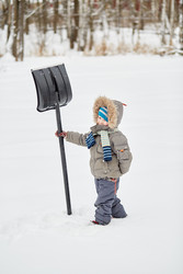 Little boy stands at snowy lawn in park, holding - paha_l