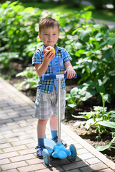 Little handsome boy eats sweet apple on scooter in - paha_l