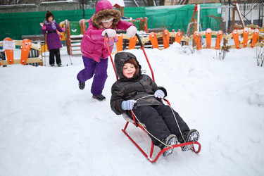 Happy girl rolling a little boy on a sled in front - paha_l