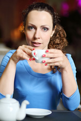 Pretty curly woman in blue dress drinks tea in - paha_l