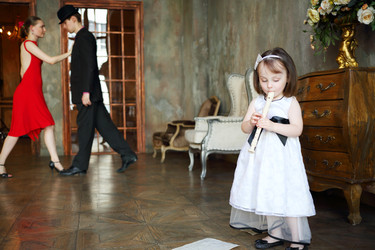 Little girl in dress plays flute in room with - paha_l