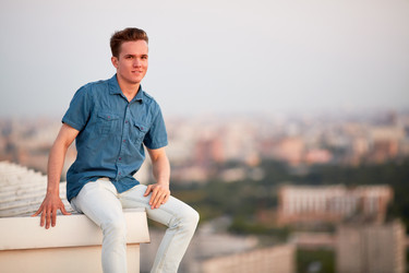 Smiling young man in denim clothes sits on the - paha_l