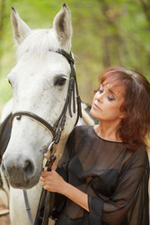 Woman in black dress stands with white horse in - paha_l