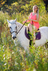 Woman in short pink dress sits on white horse in - paha_l