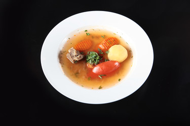 перелейте мясной бульон в белую миску. картофель, морковь, помидор, петрушка, кусочки говядины. полезный домашний суп на темном фоне - RusAKphoto