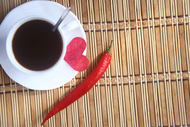 Белая чашка черного кофе с зеленым и красным острыми перцами чили и бумажное сердце на бамбуковом коврике - ZemLenik_photoclb
