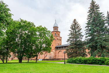 великий новгород, россия. башня кокуй новгородского детинца, высокое крепостное сооружение из красного кирпича с остроконечной крышей, историческими стенами и зелеными окрестностями в мягком свете летнего утра. - NikitaMaykov