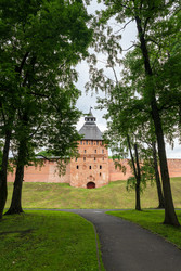 великий новгород, россия. спасская башня новгородского кремля, крепостные стены из красного кирпича и силуэт крутой крыши в обрамлении зеленых деревьев, вид с уровня улицы при мягком летнем дневном свете - NikitaMaykov
