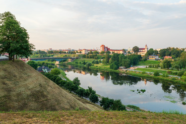 гродно, беларусь. старый мост через реку неман с голубыми металлическими пролетами и каменными опорами, панорамный вид на реку со спокойными отражениями в воде, зелеными берегами и летним утренним светом - NikitaMaykov