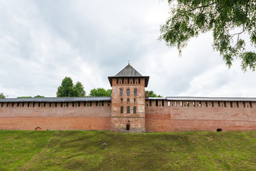 великий новгород, россия. златоустовская башня новгородского кремля, оборонительные стены из красного кирпича, арочные окна и крутая шатровая крыша открывают широкий вид летним утром под пасмурным небом - NikitaMaykov