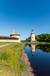 псков, россия. белокаменная плоская башня с конической деревянной крышей и цилиндрическая высокая башня охраняют слияние рек великой и псковы, отражающихся в спокойной воде - NikitaMaykov