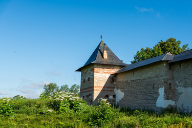 печоры, псковская область, россия. прочная башня тарарыгина псково-печерского монастыря, ее известняковые и красные кирпичные стены возвышаются над пышной зеленой летней растительностью под ясным голубым утренним небом - NikitaMaykov
